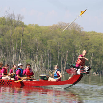 A student throws a flag into the air while riding on a red dragon boat at Big Hollow Recreation Area.