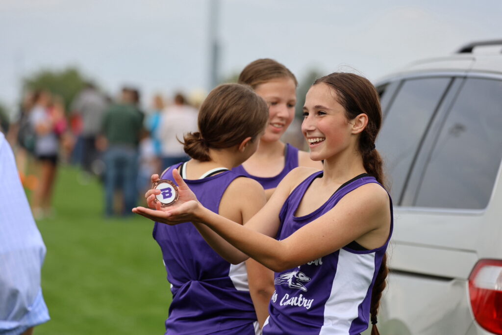 A middle school student holds up a medal she won at a cross country track meet.