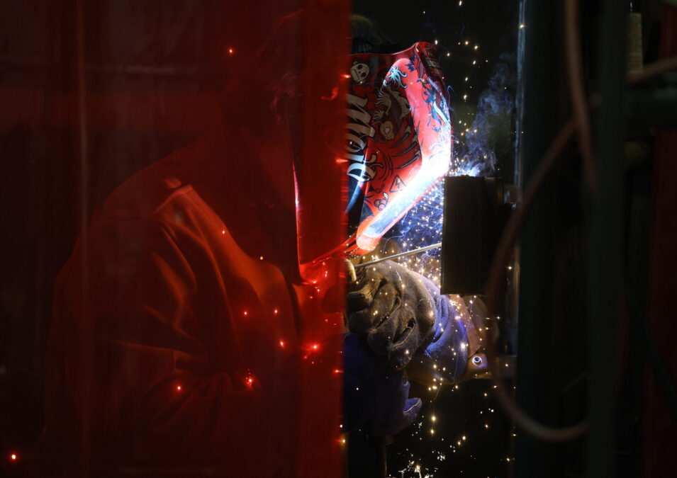 Sparks fly as a student wearing a red welding mask and gloves practices a weld at Burlington High School