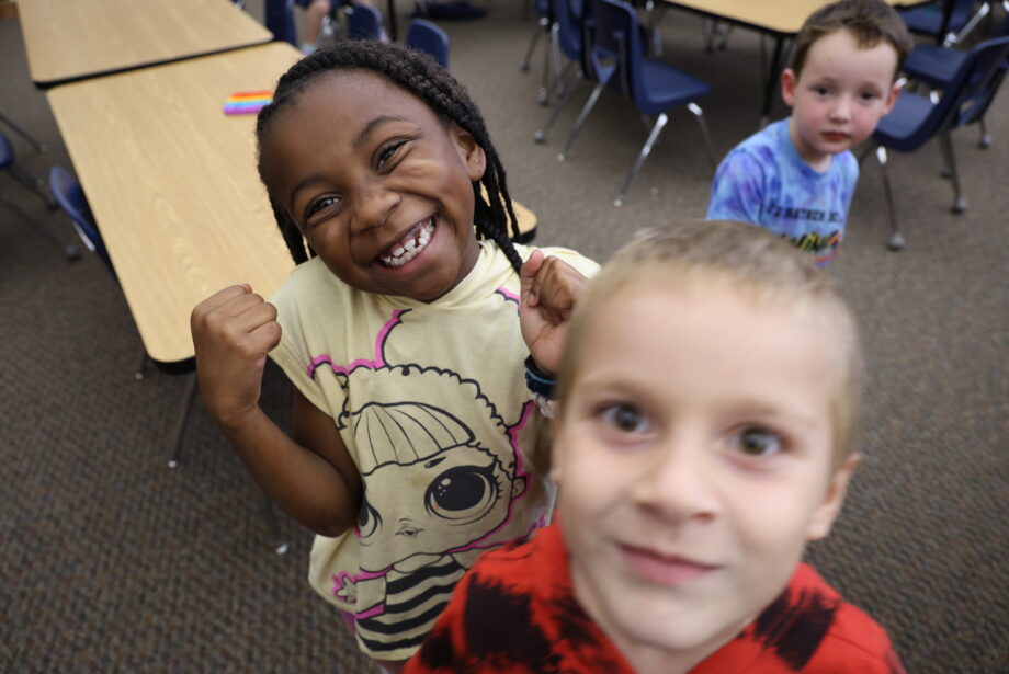 A little girl smiles at the camera alongside two boys