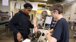 A teacher assists two students with a lathe in the metals shop at Burlington High School.