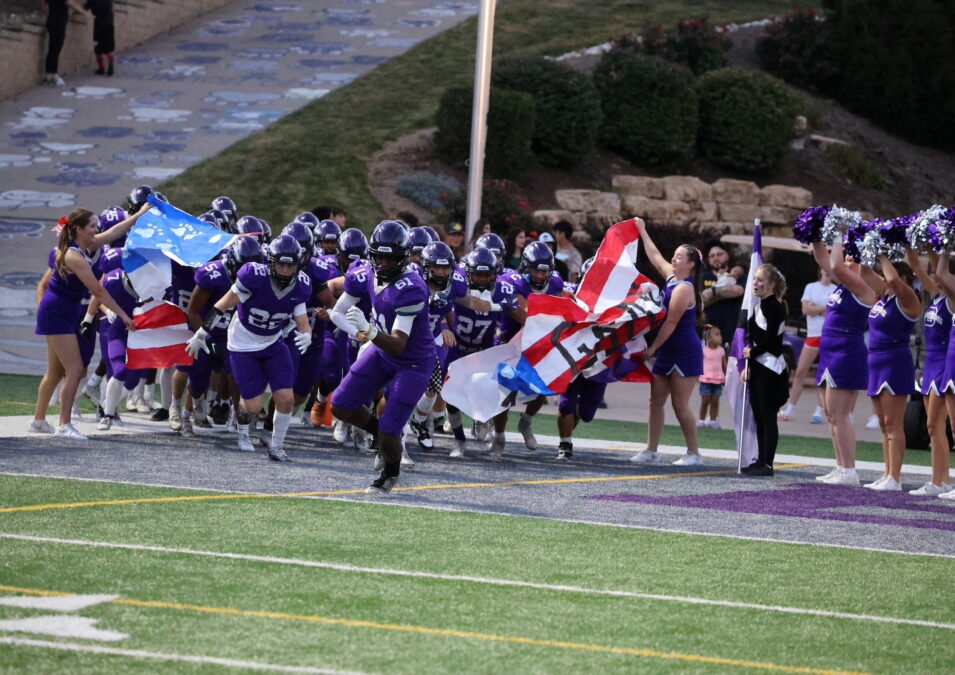 Football players burst through a banner and run onto the field at Bracewell Stadium