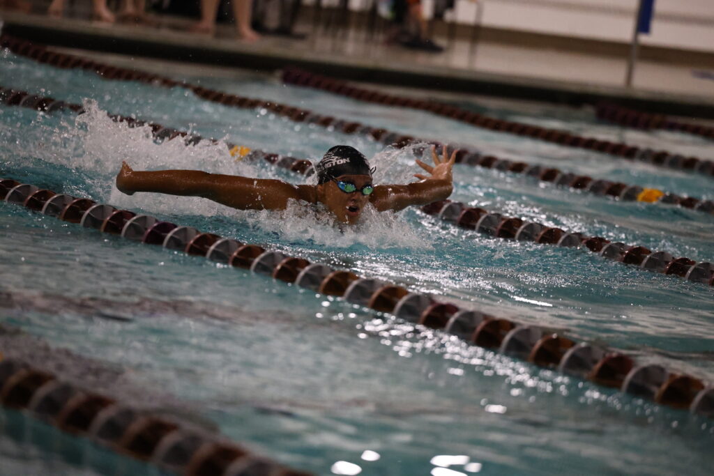 A member of the girls swim team emerges from the water while doing a butterfly stroke