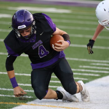 A football player holds the ball while falling to the ground to dodge a tackle from a member of the opposing team.