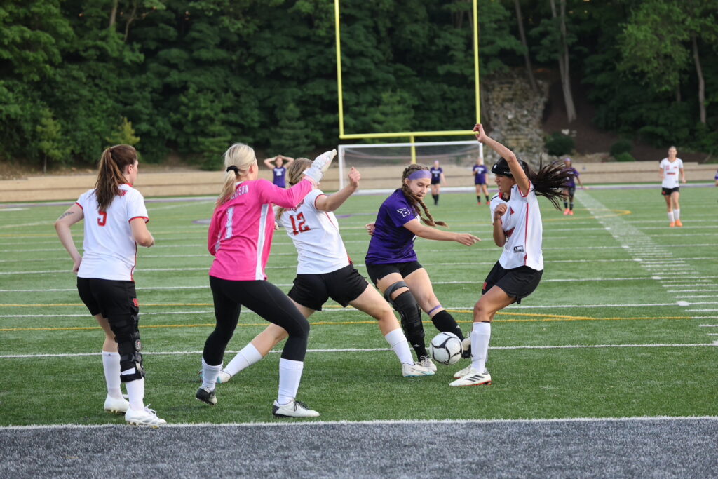 A soccer player goes to kick a ball from between her two opponents during a soccer game at Bracewell Stadium