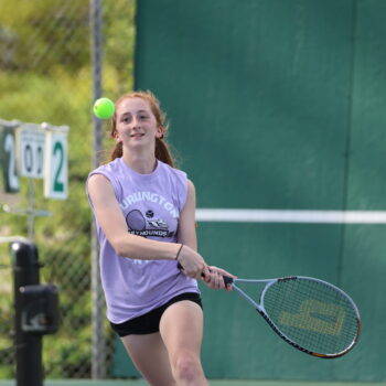 A member of the BHS JV girls tennis team goes to whack a tennis ball with her racket.