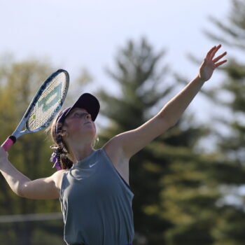 A member of the BHS girls tennis team lifts her racket to strike a ball.