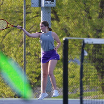 A member of the BHS girls tennis team lifts her racket to strike a ball.