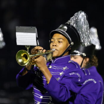 A student plays the trumpet with the marching band during a football halftime show.