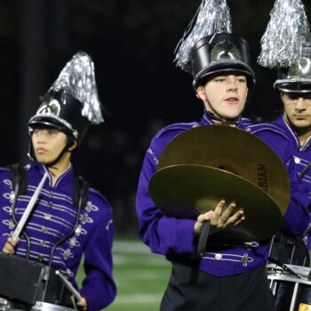 A student plays two cymbals with the marching band during a football halftime show.