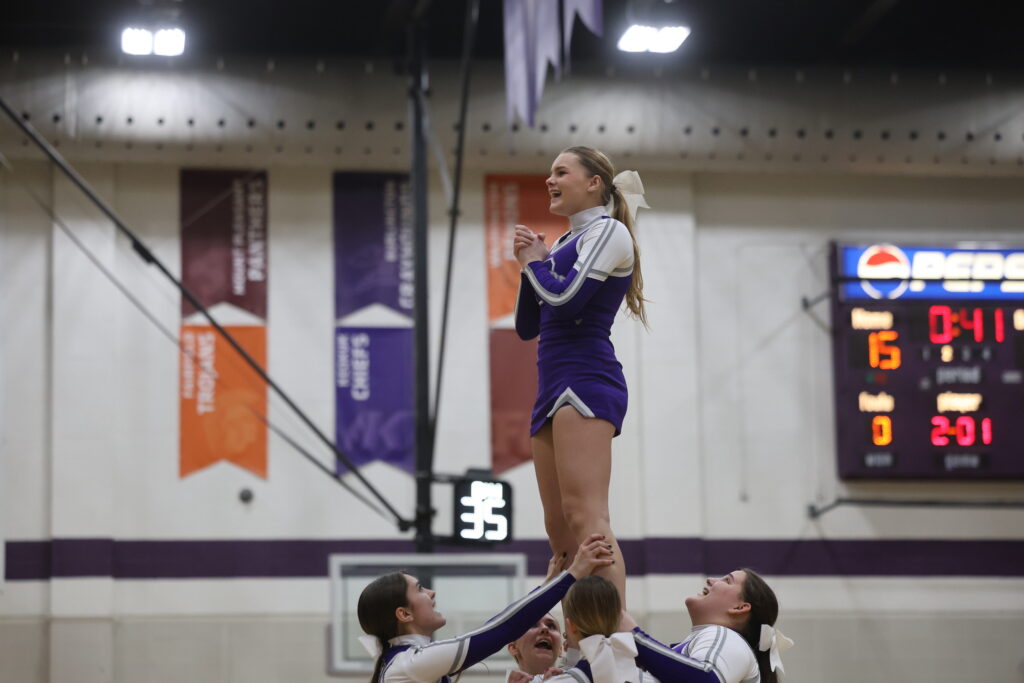 A group of cheerleaders lift another cheerleader in the air during a basketball game