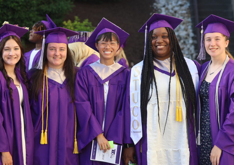 Five girls wearing purple cap and gown pose for a photo ahead of their graduation ceremony