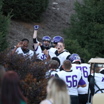 Members of the JV football team cheer while ringing the victory bell at Bracewell Stadium.