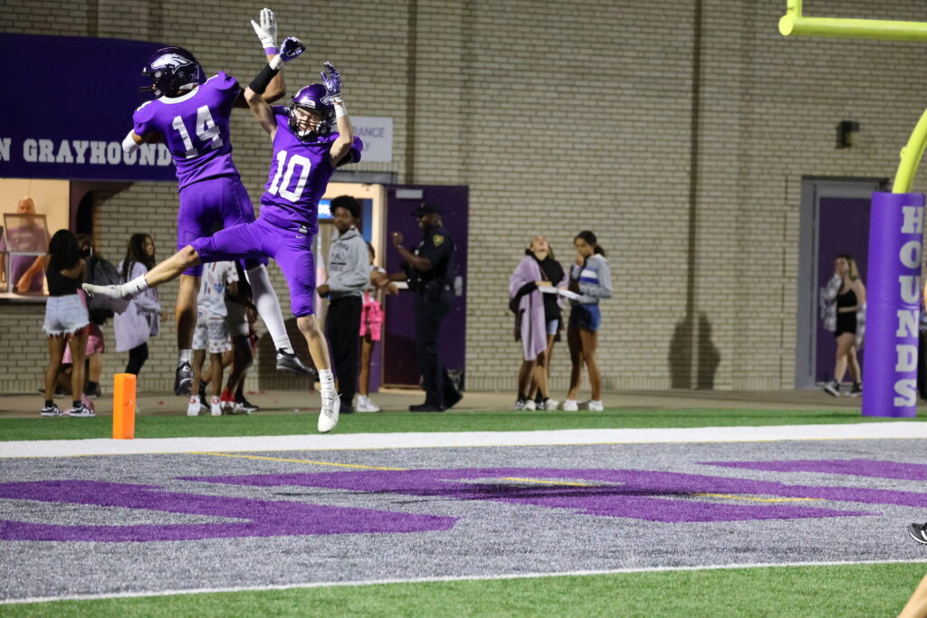 Two football players jump in the air after their team scores a touchdown during a football game.