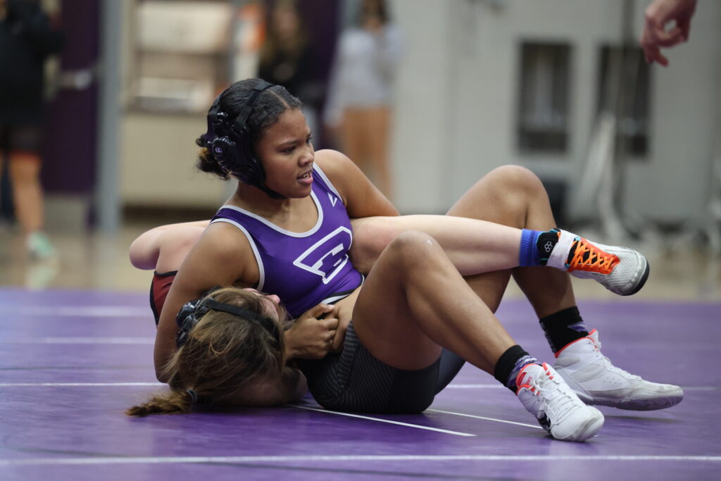 A member of the girls wrestling team holds her opponent down on the mat. 