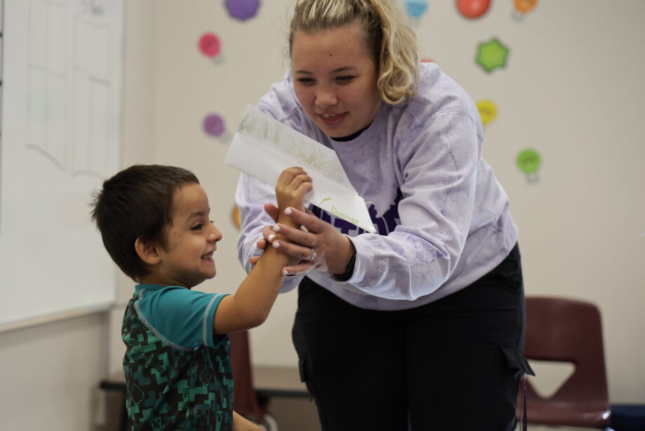 A teacher helps a kindergarten boy adjust his grip on a paper airplane he made