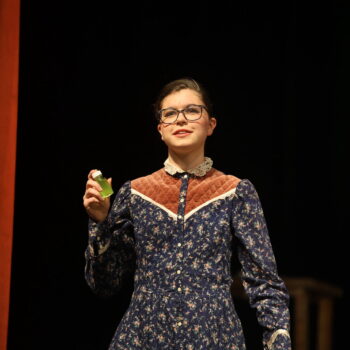 A student actor holds up a vile of glowing green liquid during the spring play, 