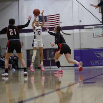 A member of the girls basket ball team goes for a basket as two members of the opposing team run toward her.