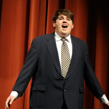 A student actor wearing a suit and tie sings during the fall production of 