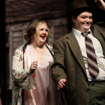 A student actress dressed as Ms. Hannigan sings alongside another student actress wearing a suit and tie during the fall production of 