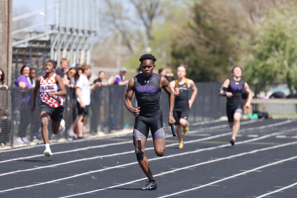 A member of the boys track and field team outruns his opponents on the track