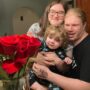 Allison Cook poses for a photo with her son and fiance next to a bouquet of roses.