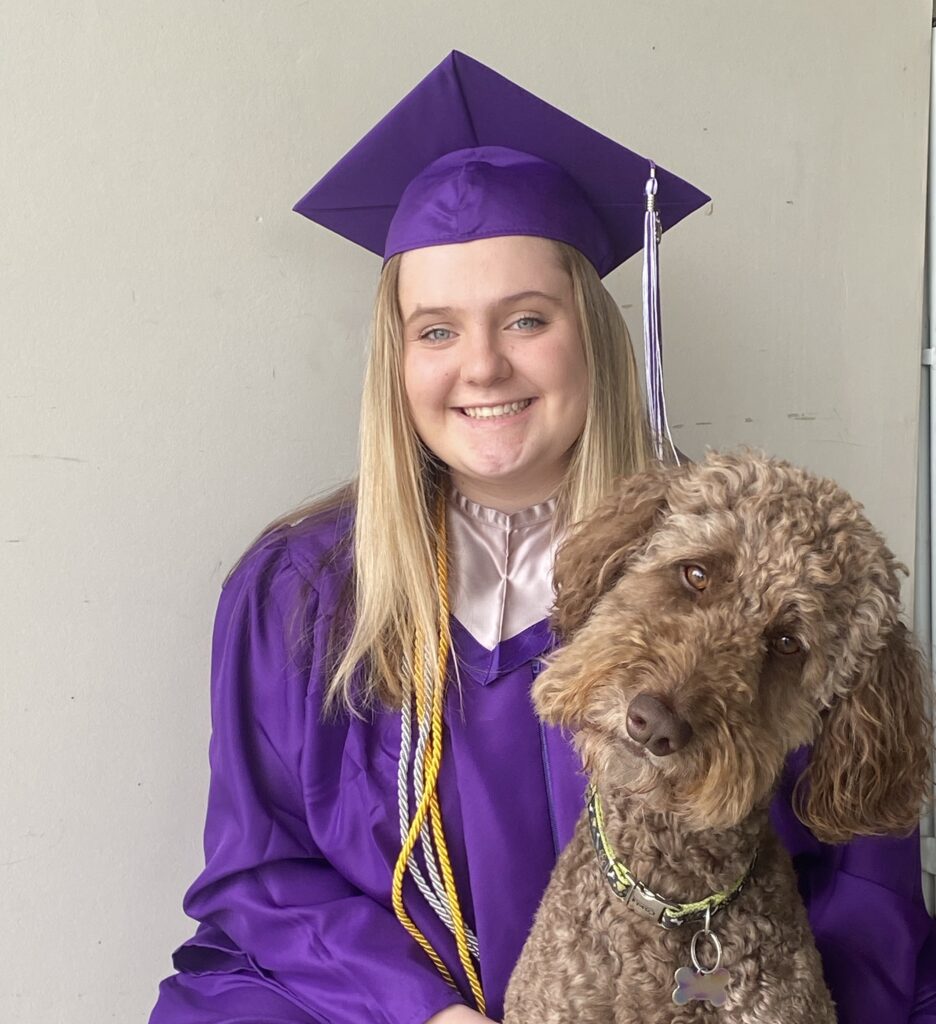 Taylor Kesterke poses for a photo in cap and gown with her dog.