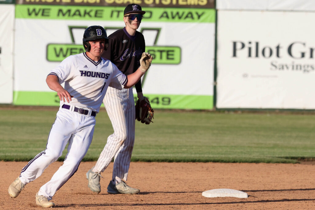 A baseball player puts his arm up as he reaching for the ball on the ball field.