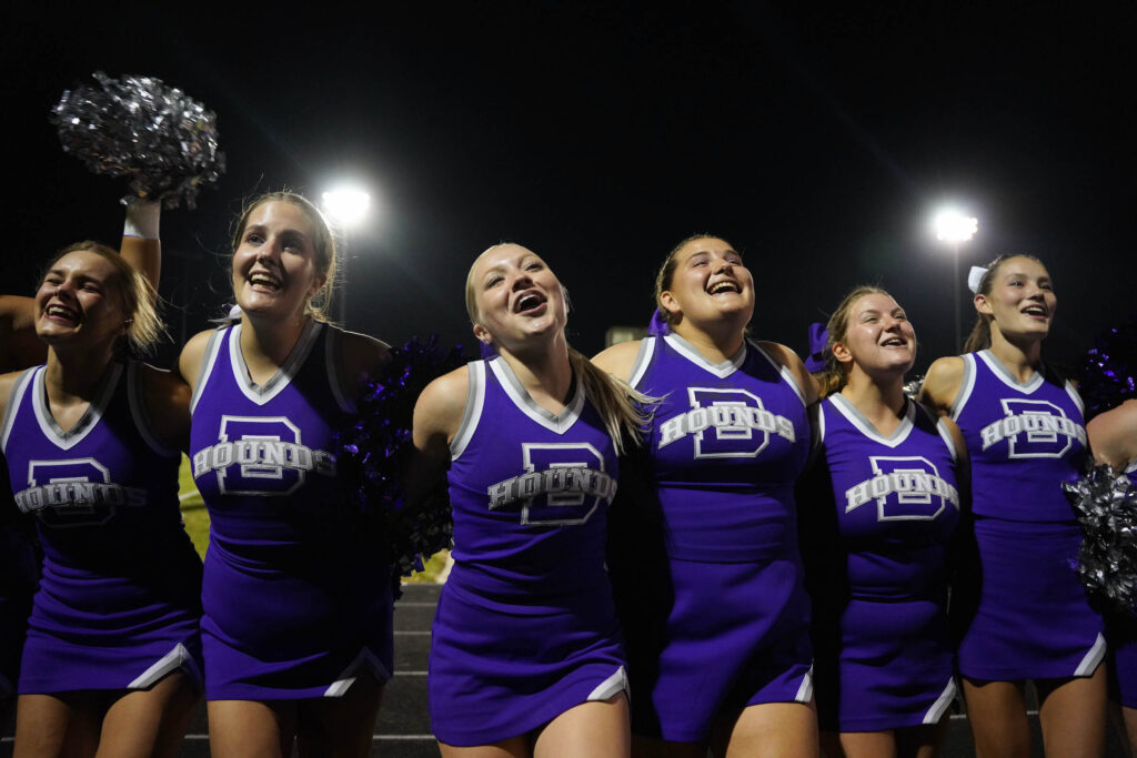 Six cheerleaders lead a crowd in a cheer during a football game