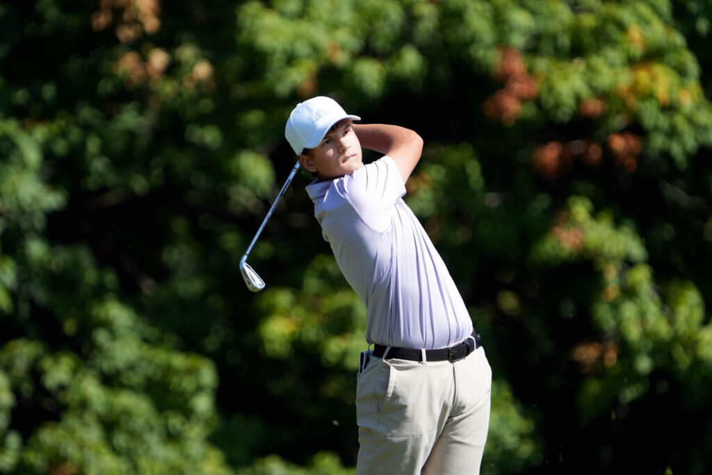 A member of the boys golf team watches his ball after swinging his club.