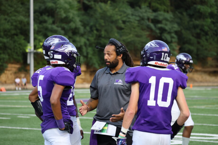 Burlington High School's new head football coach, Jordan Webb, talks to three football players on the football field at Bracewell Stadium.