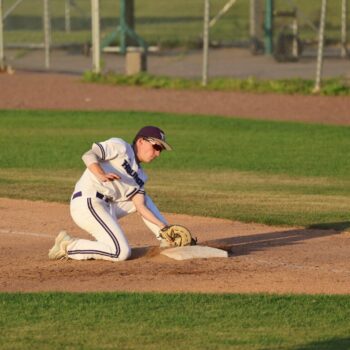 A baseball player bends down to pick up the ball by a base.