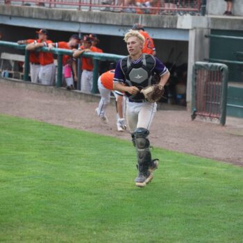 A catcher makes his way back to the home plate after catching a foul ball during a baseball game.