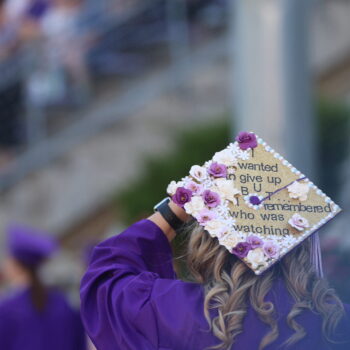 A young woman wears a graduation cap displaying the words, 