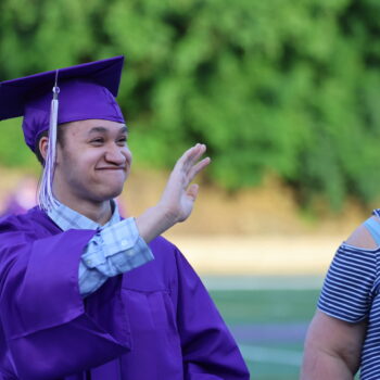 A graduating senior smiles while waving to someone he knows ahead of the 2024 commencement ceremony at Bracewell Stadium.