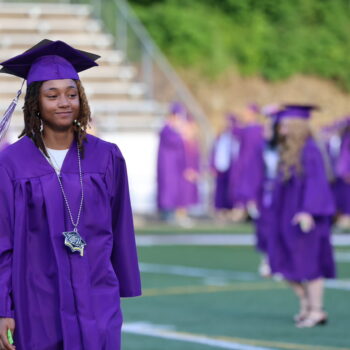 A graduating senior wears a slight smile while making her way to her seat at the start of the 2024 commencement ceremony at Bracwell Stadium.