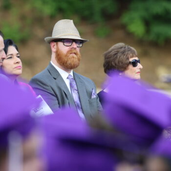 School board members and district administrators sit on stage in front of a sea of purple caps during the 2024 commencement ceremony at Bracewell Stadium.