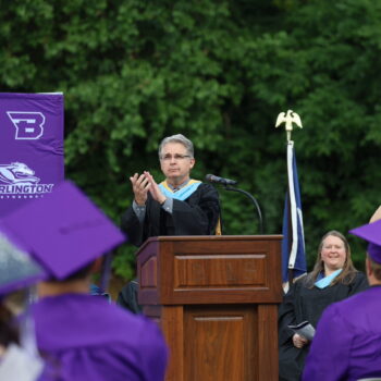 Superintendent Robert Scott claps while standing behind a podium and in front of the graduating class of 2024 during the commencement ceremony at Bracewell Stadium.