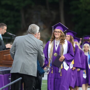 The salutatorian shakes hands with a school board member after accepting her diploma during the 2024 commencement ceremony at Bracewell Stadium.