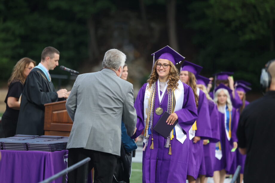 The salutatorian shakes hands with a school board member after accepting her diploma during the 2024 commencement ceremony at Bracewell Stadium.