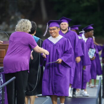 A graduate shakes the hand of a school board member after accepting his diploma during the 2024 commencement ceremony at Bracewell Stadium.