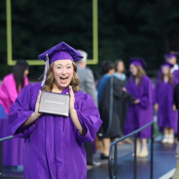 A graduate proudly displays her diploma after walking across the stage at the 2024 Commencement Ceremony at Bracewell Stadium.