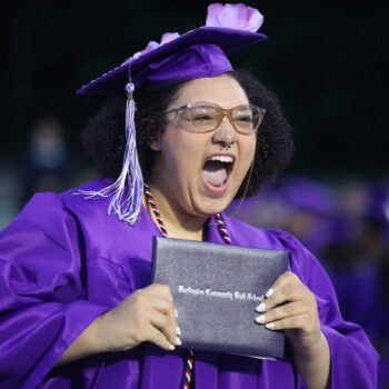 A young woman excitedly holds her diploma after walking across the stage during the 2024 commencement ceremony.