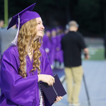 A young woman smiles while walking back to her seat after receiving her diploma during the 2024 commencement ceremony at Bracewell Stadium.