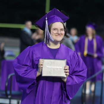 A graduate proudly displays her diploma after walking across the stage at the 2024 Commencement Ceremony at Bracewell Stadium.