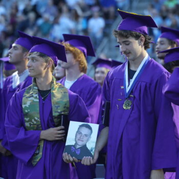 Two graduates hold up a photo of their fallen classmate during the 2024 commencement ceremony at Bracewell Stadium.