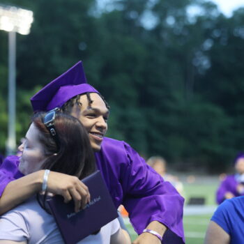 A BHS graduate smiles while hugging a loved one and holding his diploma following the 2024 commencement ceremony at Bracwell Stadium.