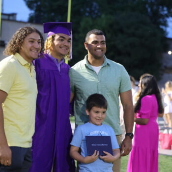 A graduate stands with his family for a photo while his younger sibling holds up his diploma following the 2024 commencement ceremony at Bracewell Stadium.