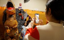 A parent takes a photo of her daughters next to an inflatable dinosaur Oct. 29, 2024, at Edward Stone Middle School during the Haunted Halls event.