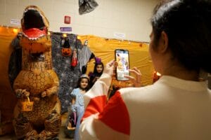 A parent takes a photo of her daughters next to an inflatable dinosaur Oct. 29, 2024, at Edward Stone Middle School during the Haunted Halls event.